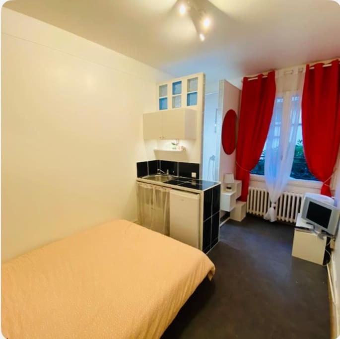 Cet appartement comprend une chambre avec un lit et une cuisine avec des rideaux rouges. dans l'établissement jolie studette équipée st mande proche bois et transports, à Saint-Mandé