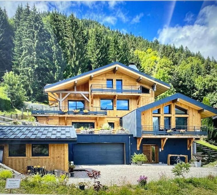 une grande maison en bois avec un garage bleu dans l'établissement Stunning apartment- mountain views near Morzine, à La Côte dʼArbroz