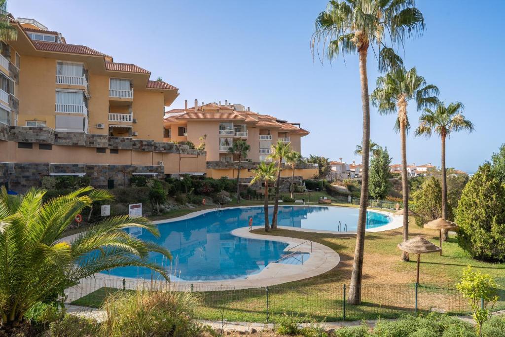 ein Swimmingpool vor einem Gebäude mit Palmen in der Unterkunft Higuerón Hills Retreat - Home in Benalmádena in Fuengirola
