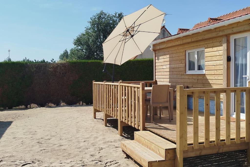 a wooden deck with a table and an umbrella at BERCK-PLAGE - Location saisonnière Tiny House insolite - 4 hébergements atypiques avec terrasse privée, proche mer, parking privé et gratuit, idéal weekend romantique, vacances en famille ou groupe in Berck-sur-Mer