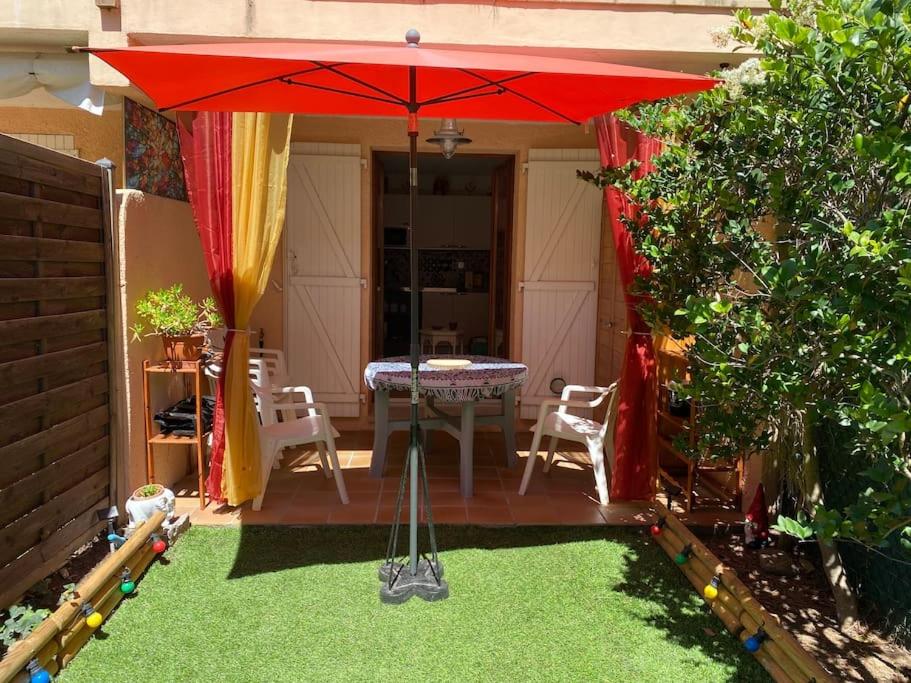 d'une terrasse avec une table et un parasol rouge. dans l'établissement joli appartement avec jardin, à Cavalaire-sur-Mer