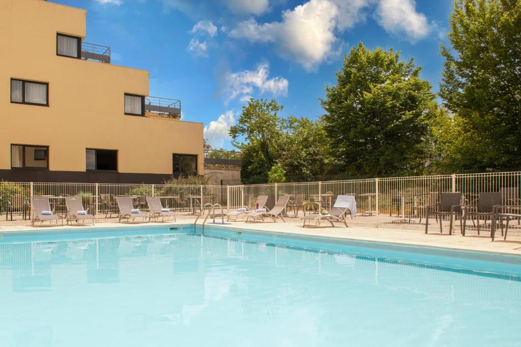une piscine avec des chaises et un bâtiment en arrière-plan dans l'établissement The Originals City, Hôtel Alteora, Poitiers Site du Futuroscope, à Chasseneuil-du-Poitou
