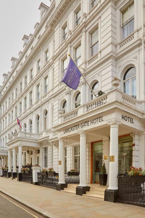 ein großes weißes Gebäude mit einer lila Flagge darauf in der Unterkunft Lancaster Gate Hotel in London