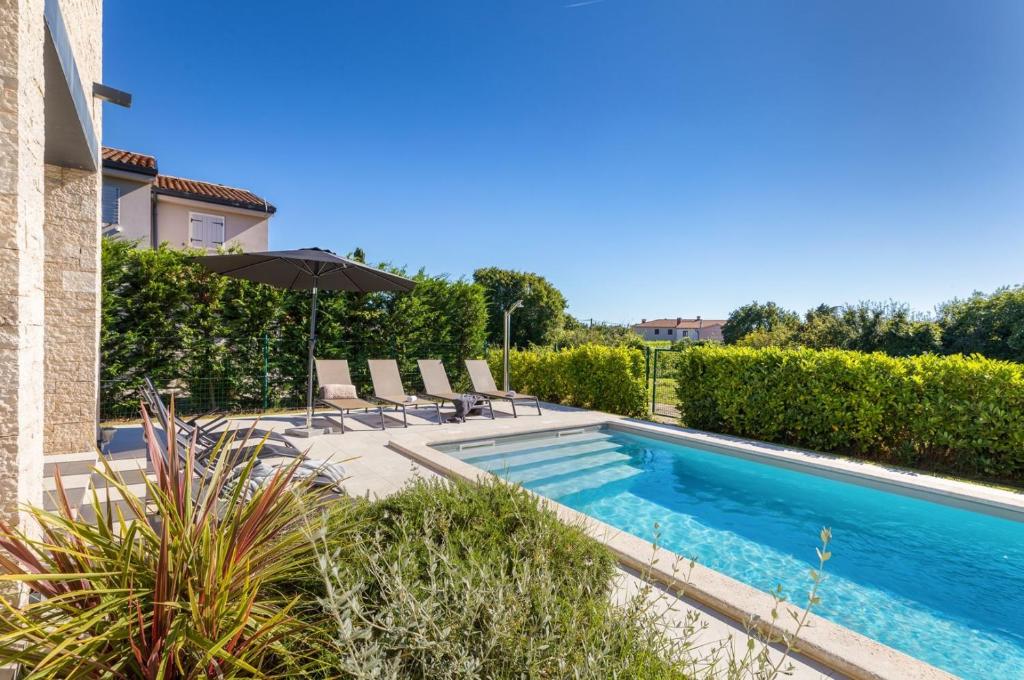 a swimming pool with chairs and an umbrella next to a house at Villa Calma in Šivati