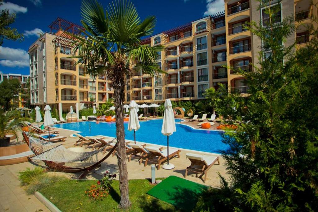 a hotel swimming pool with a palm tree and chairs and umbrellas at Harmony Suites Jungle - Apartment Veron in Sunny Beach