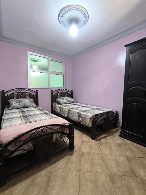 two beds in a room with purple walls and a window at Appartement a Martil in Martil