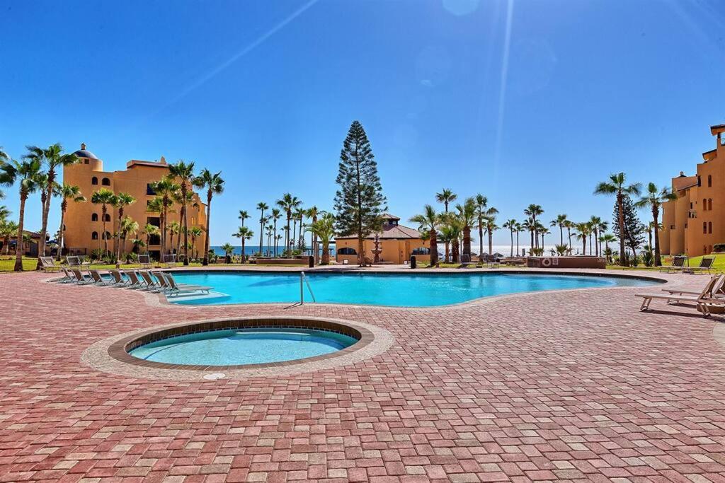 a swimming pool with chairs and trees in a resort at Sandy Beach Princesa D107 Ocean Front Resort in Puerto Peñasco