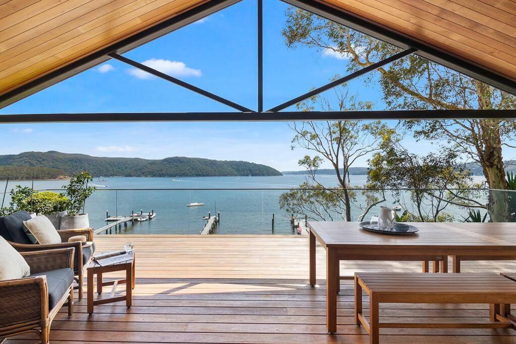 a view from the deck of a house with a large glass window at Island Style - By Betina King in Scotland Island