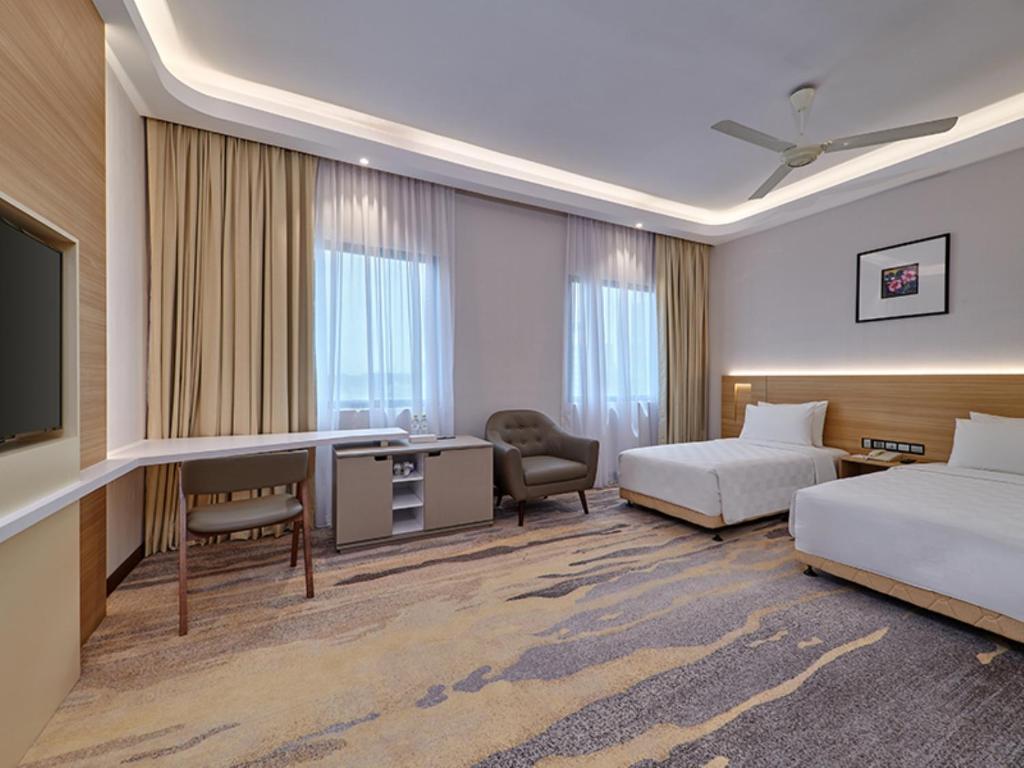 A spacious twin-bed room includes a desk, television, armchair and large curtained windows.