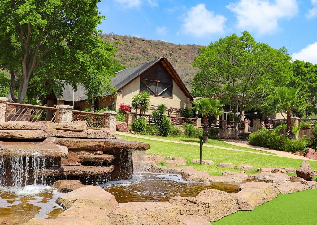a waterfall in front of a yard with a house at Olifants River Lodge by Dream Resorts in Middelburg