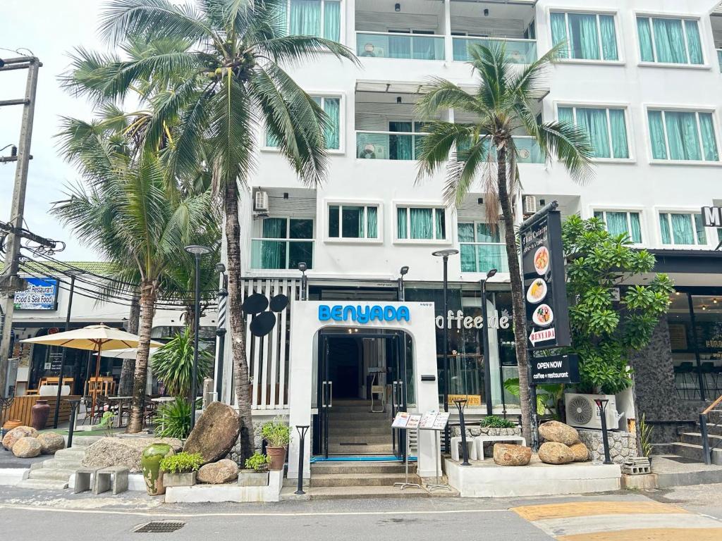 a hotel with palm trees in front of a building at Benyada Lodge - Surin Beach in Surin Beach