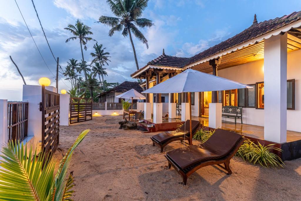 a house with chairs and an umbrella in front of it at Villa Naina, Marari beach in Alleppey