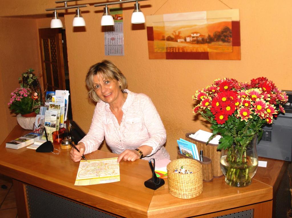 an older woman sitting at a counter with flowers at Hotel-Pension Grüne Linde in Delitzsch