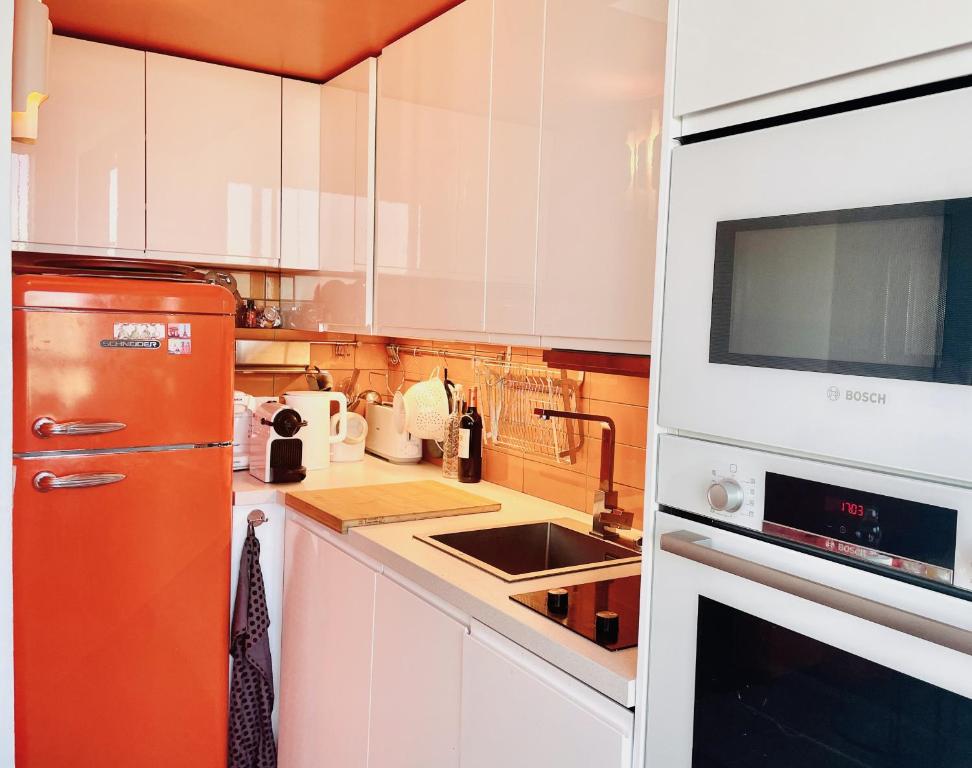 a kitchen with white cabinets and an orange refrigerator at Panoramique vue NEW design proche Tour Eiffel in Paris