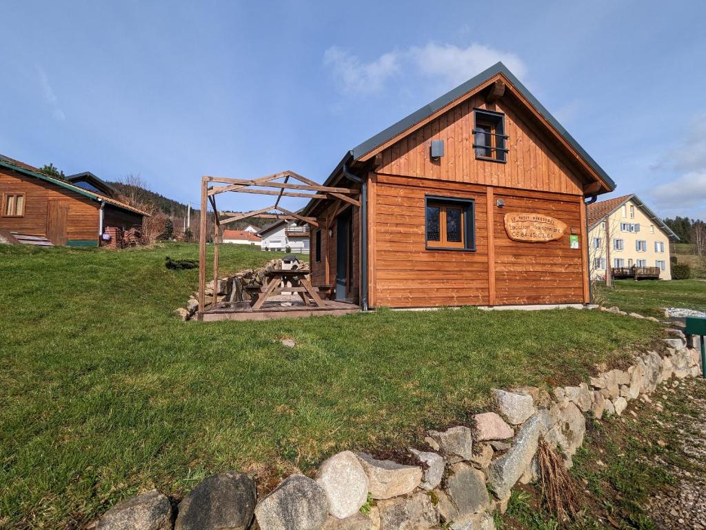a wooden house in a field with a stone wall at Chalet neuf à Gérardmer avec terrasse et parking privé - FR-1-589-465 in Gérardmer