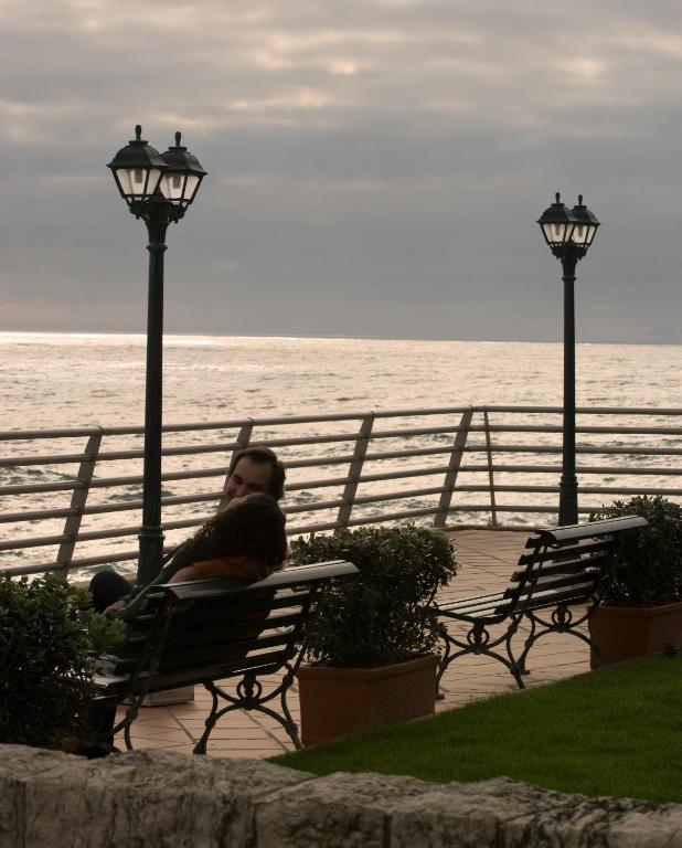 a man sitting on a bench next to the ocean at Vila Gale Ericeira in Ericeira