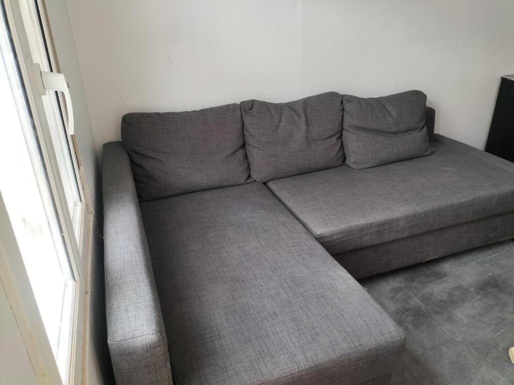 - un canapé gris dans le salon à côté d'une fenêtre dans l'établissement Loft avec chambre, tout confort pour les jo ou visiter Paris, à Aubervilliers