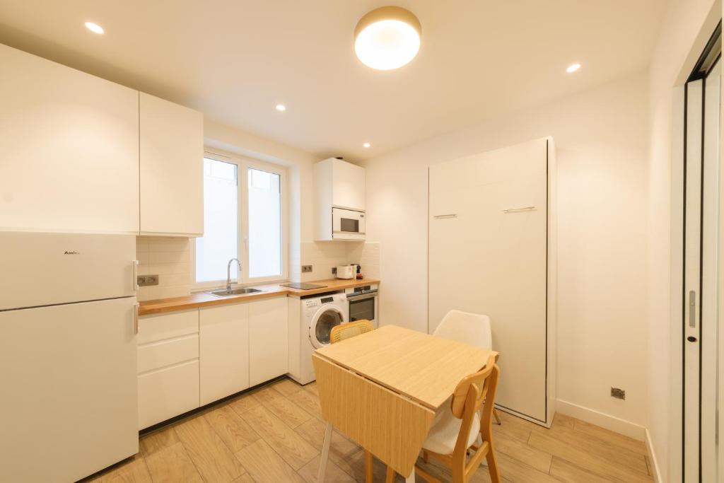 une cuisine avec des armoires blanches et une table avec des chaises dans l'établissement Cosy apartment 3P - Place de l'Etoile, à Paris