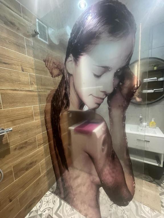 a woman in a shower holding a cell phone at APARTAMENT KRÓLEWSKI CENTRUM NIEPOŁOMICE in Niepołomice