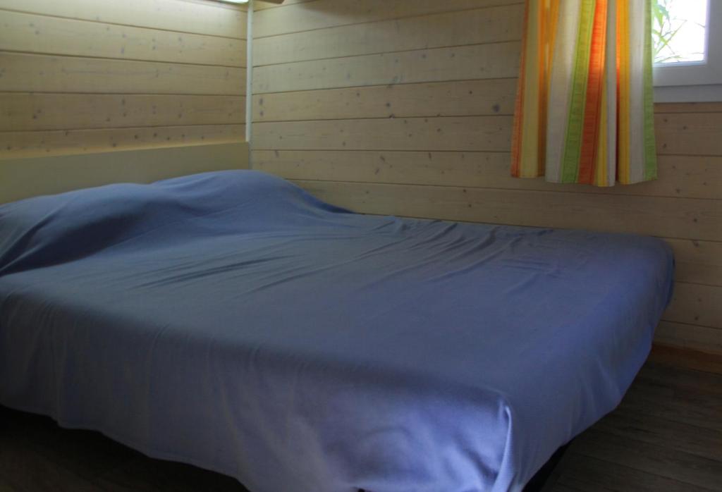 een bed in een houten kamer met een raam bij Camping Hameau Des Cannisses in Gruissan