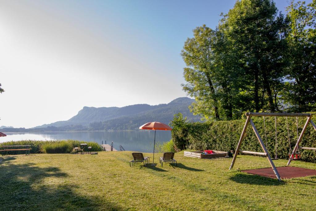 a playground with an umbrella and chairs and a swing at Ferienwohnungen Gabriel in Keutschach am See