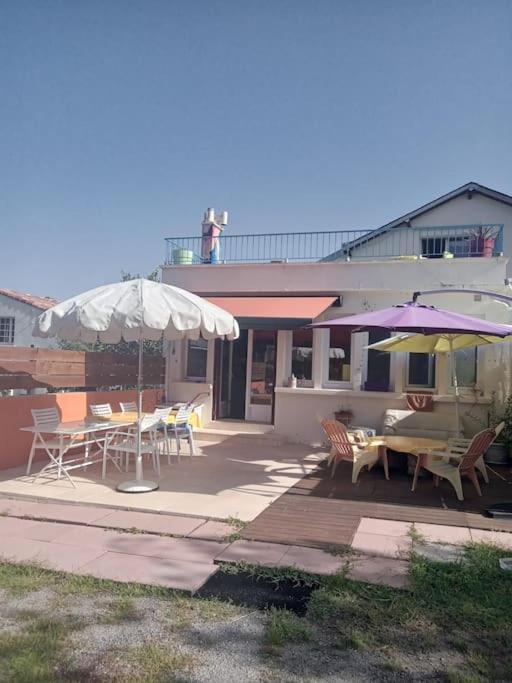 une terrasse avec des tables et des parasols en face d'une maison dans l'établissement Grande maison familiale spacieuse , agréable et calme, à Landeronde