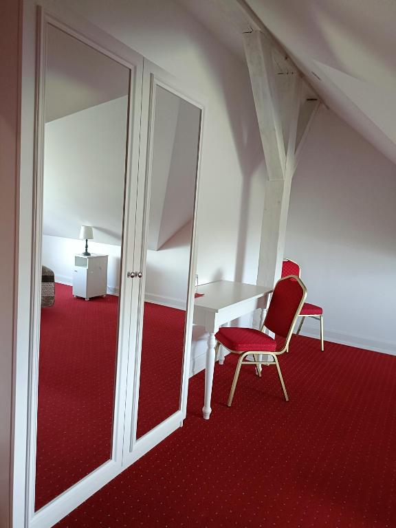 Attic bedroom corner with mirrored wardrobe, white desk and two red chairs on red carpet.