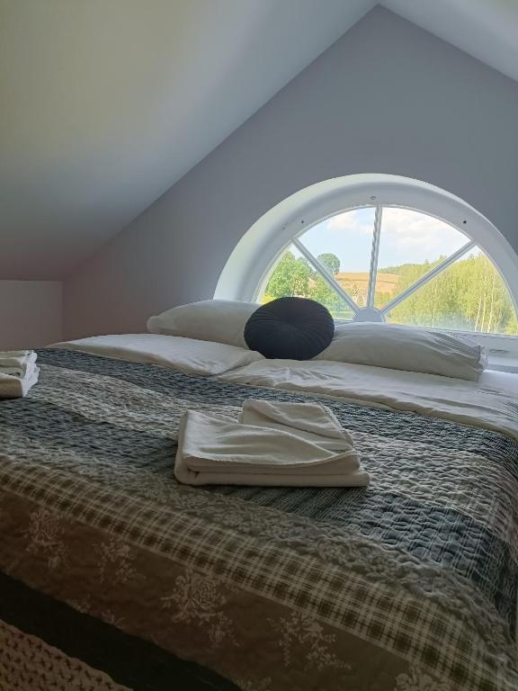 Cozy loft bedroom with large bed, folded towels on quilt and round bolster, arched window view.