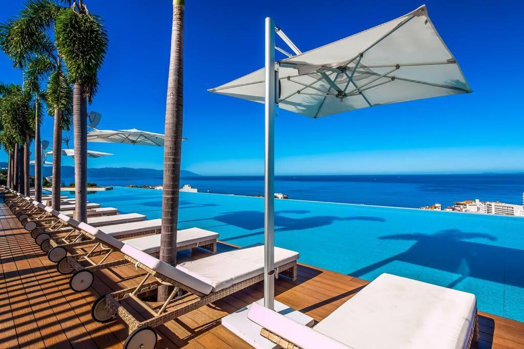 a row of lounge chairs and an umbrella on a swimming pool at SOHO PV - 1007 Best and Brand New Condo in Puerto Vallarta