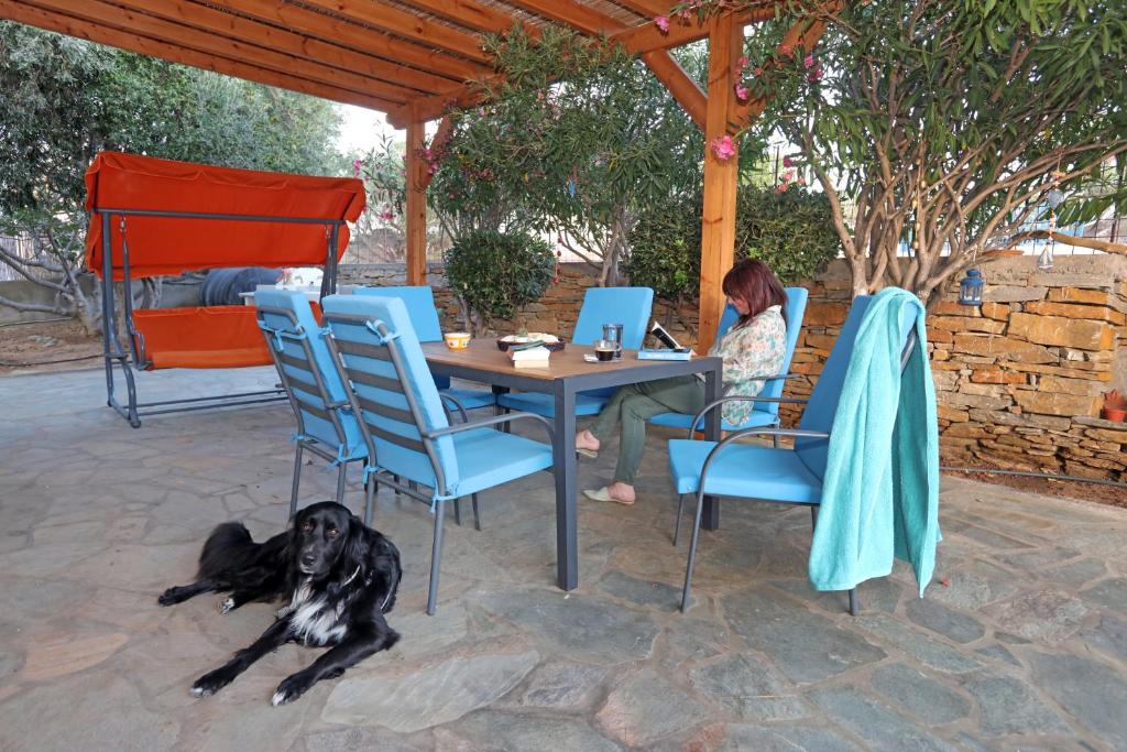a woman sitting at a table with a dog laying on the ground at Ruby's summer house with spacious garden and free parking in Gavrio