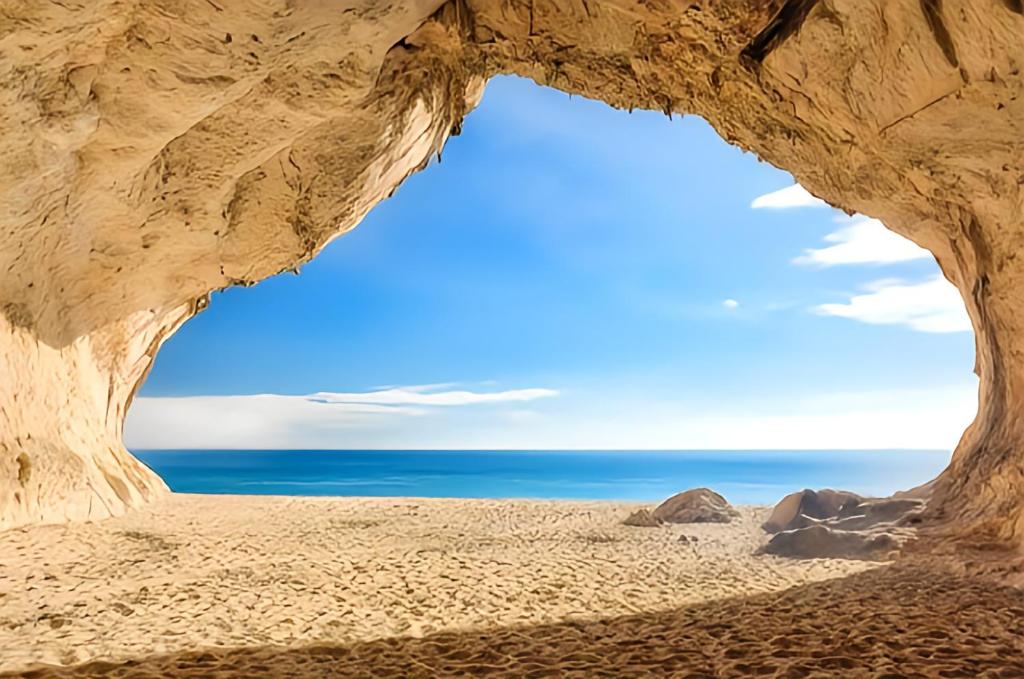 a cave on the beach with the ocean in the background at La Grotta Sardegna 4 Bedrooms in Urzulei
