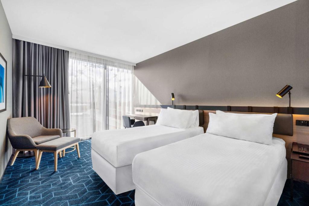 a hotel room with two beds and a chair at Vibe Hotel Melbourne Docklands in Melbourne