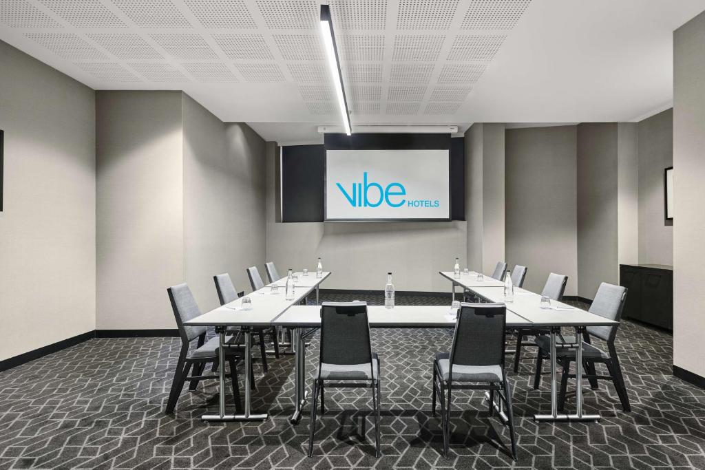 a conference room with tables and chairs and a screen at Vibe Hotel Melbourne Docklands in Melbourne