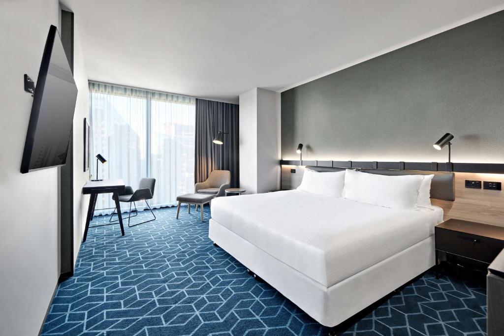 a hotel room with a large white bed and a desk at Vibe Hotel Melbourne Docklands in Melbourne