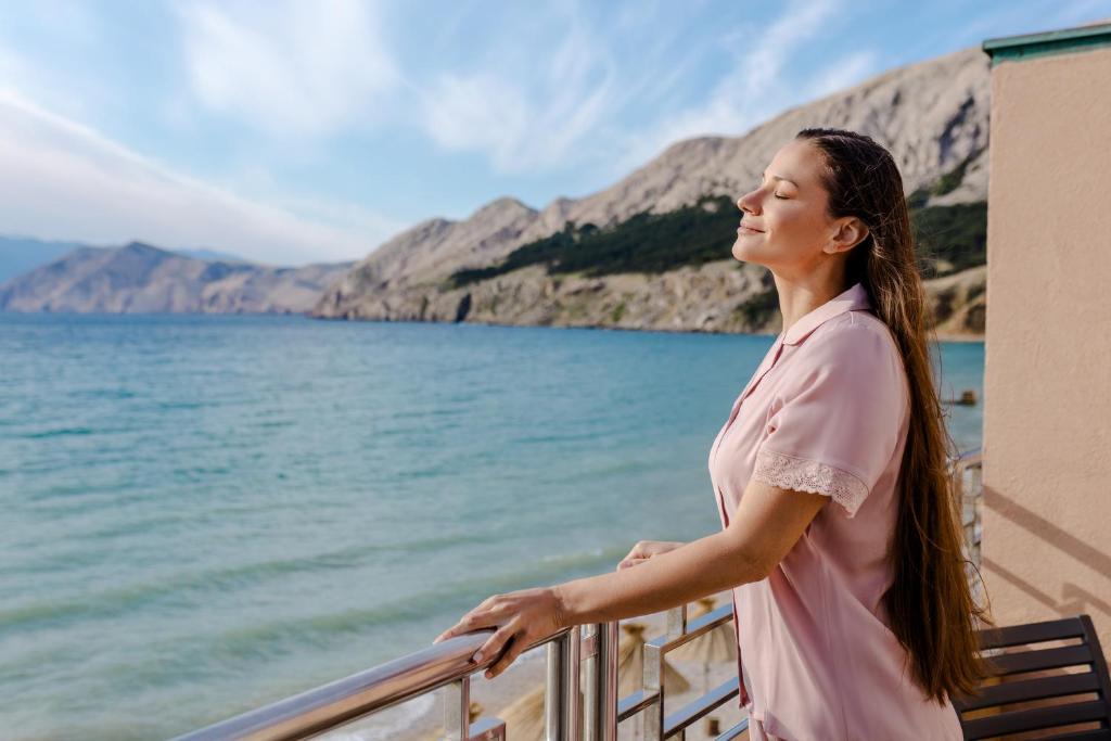 a woman standing on a balcony overlooking the water at Hotel Dobrovit in Baška