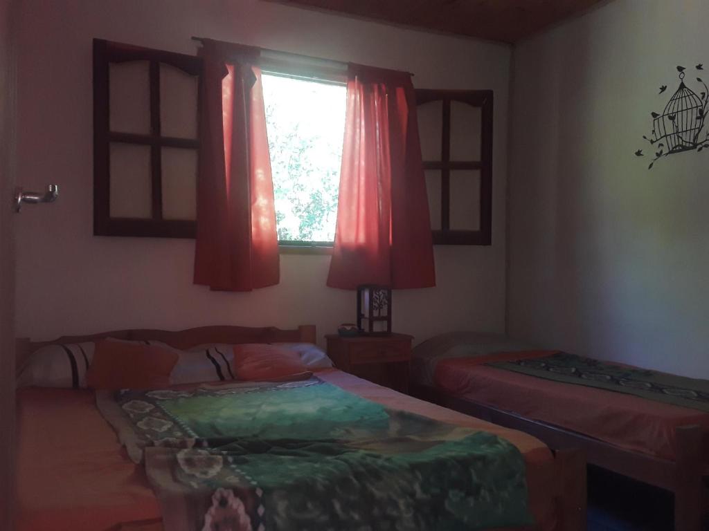 - une chambre avec 2 lits et une fenêtre avec des rideaux rouges dans l'établissement Cabañas La Fiaca, à Los Manantiales