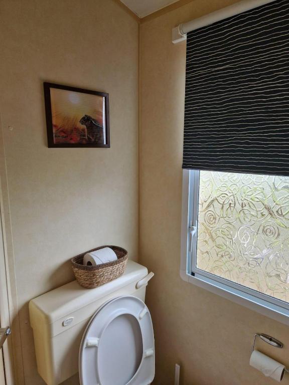 a bathroom with a toilet with a window and a basket on it at Lochview Retreat Caravan in Balminnoch
