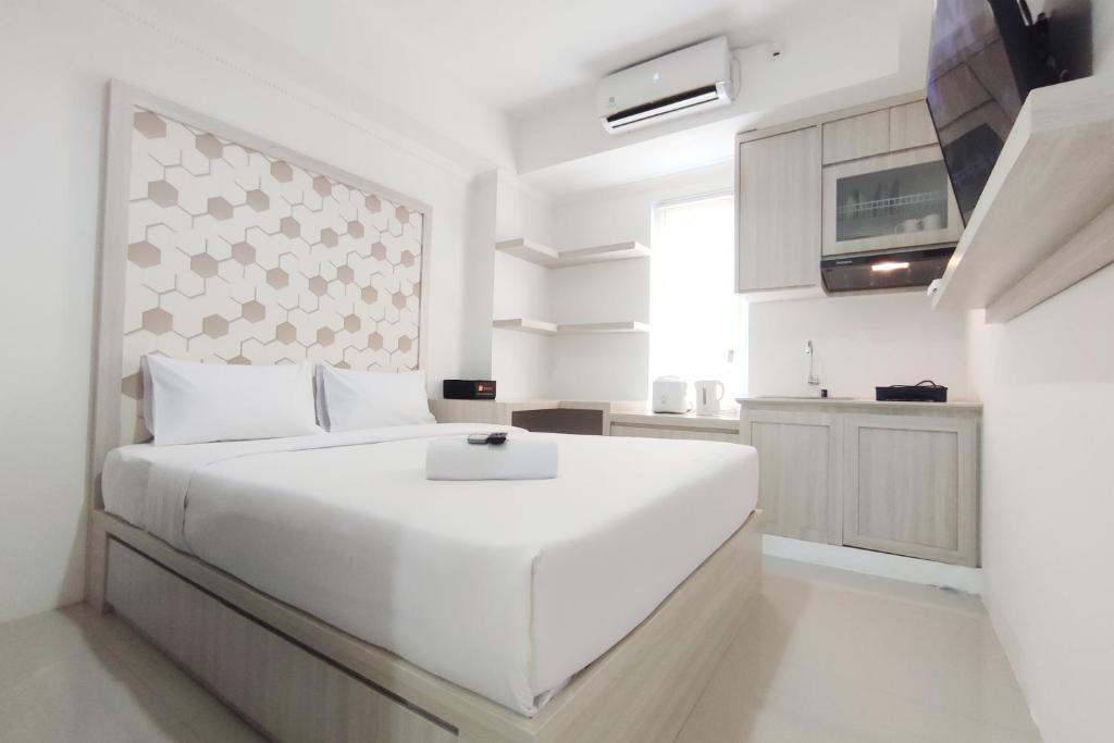 a white bedroom with a large white bed and a kitchen at Nice Cozy Studio at Paltrow City Apartment By Travelio in Semarang