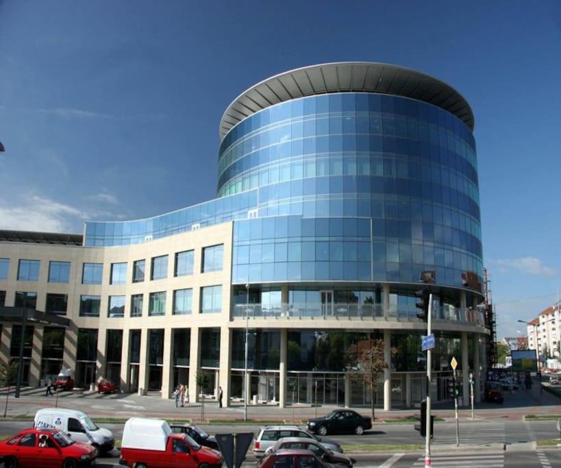 a large glass building with cars parked in a parking lot at Lovely apartment near NS Fair in Novi Sad