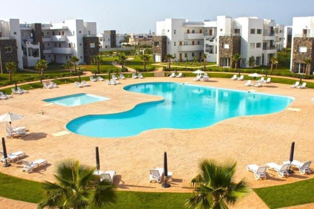 a large swimming pool with chairs and palm trees at PERLA SAÏDIA APPART XXL Clima IPTV Piscine Parking Jardin in Saidia 