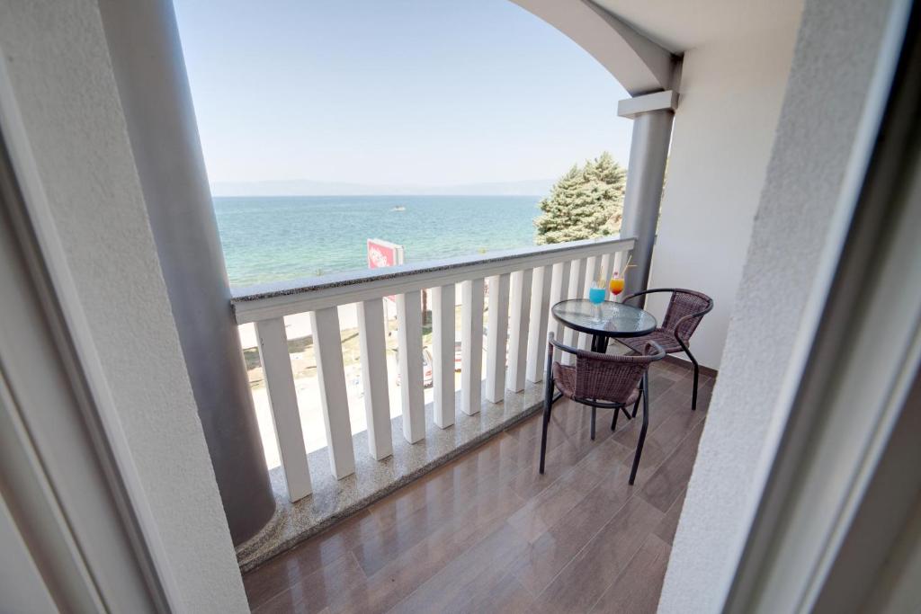 Private balcony with glass-top table, two wicker chairs and drink, overlooking the sea and distant beach at City Palace Hotel in Ohrid