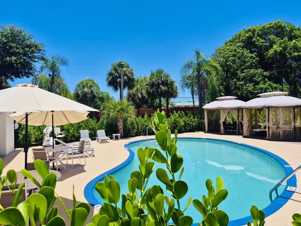 a pool with umbrellas and tables and chairs at Nova Inn Resort in Boynton Beach