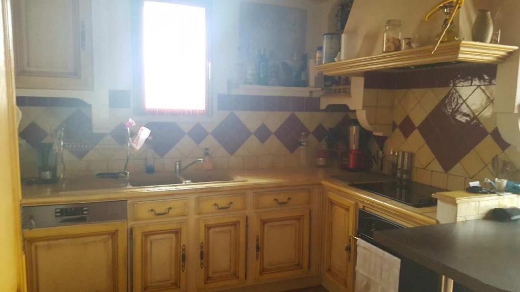 une cuisine avec des armoires en bois, un évier et une fenêtre dans l'établissement Maison de village dans Languedoc-Roussillon, à Vergèze
