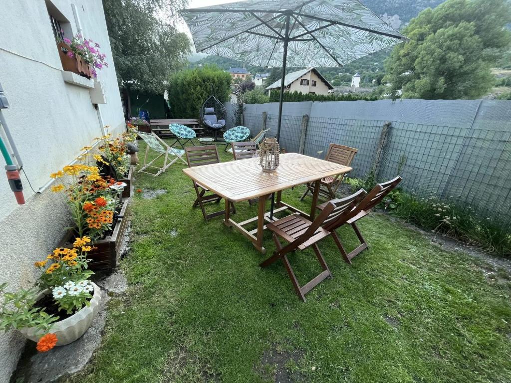 a wooden table and chairs in a yard with flowers at Appartement spacieux à L'Argentière-la-Bessée, terrasse et jardin in LʼArgentière-la-Bessée