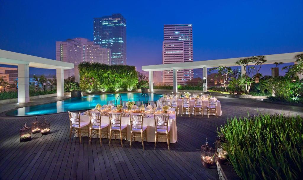 a group of tables and chairs on a deck with a pool at Mandarin Oriental, Jakarta in Jakarta