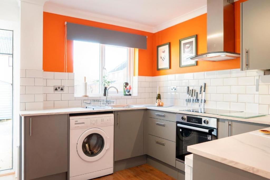 an orange kitchen with a washing machine in it at Stylish 2 BR Parking 7 mins Oxford 14 Bicester in Kidlington
