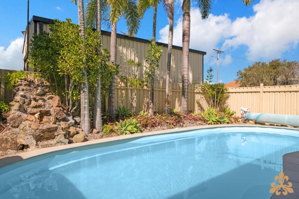 Una piscina frente a una valla con palmeras. en Oasis On Rice Street Downstairs, en Rockhampton