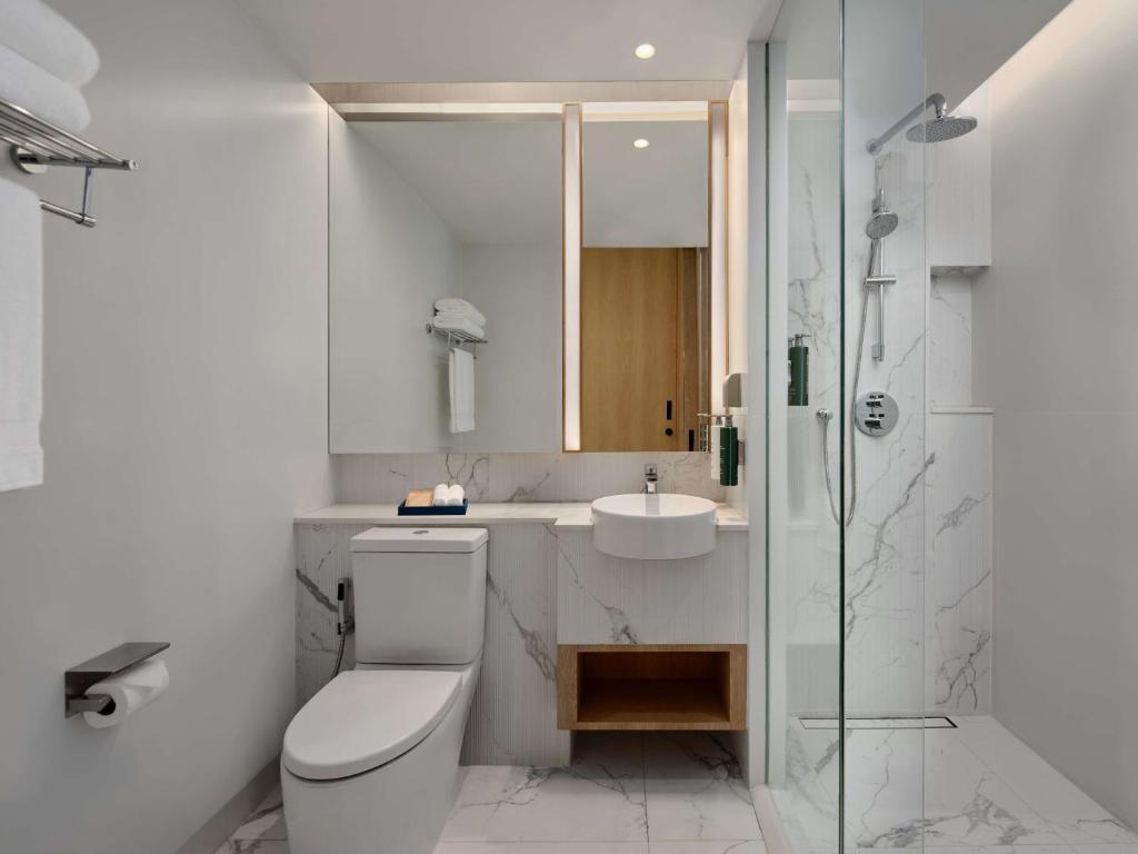 A bright marble-look bathroom with a toilet, floating sink and enclosed glass shower.