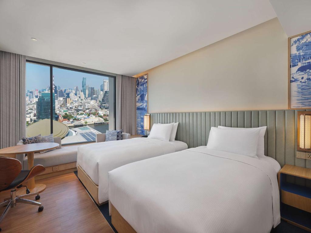 A twin room with two beds, a desk and a large city-facing window.