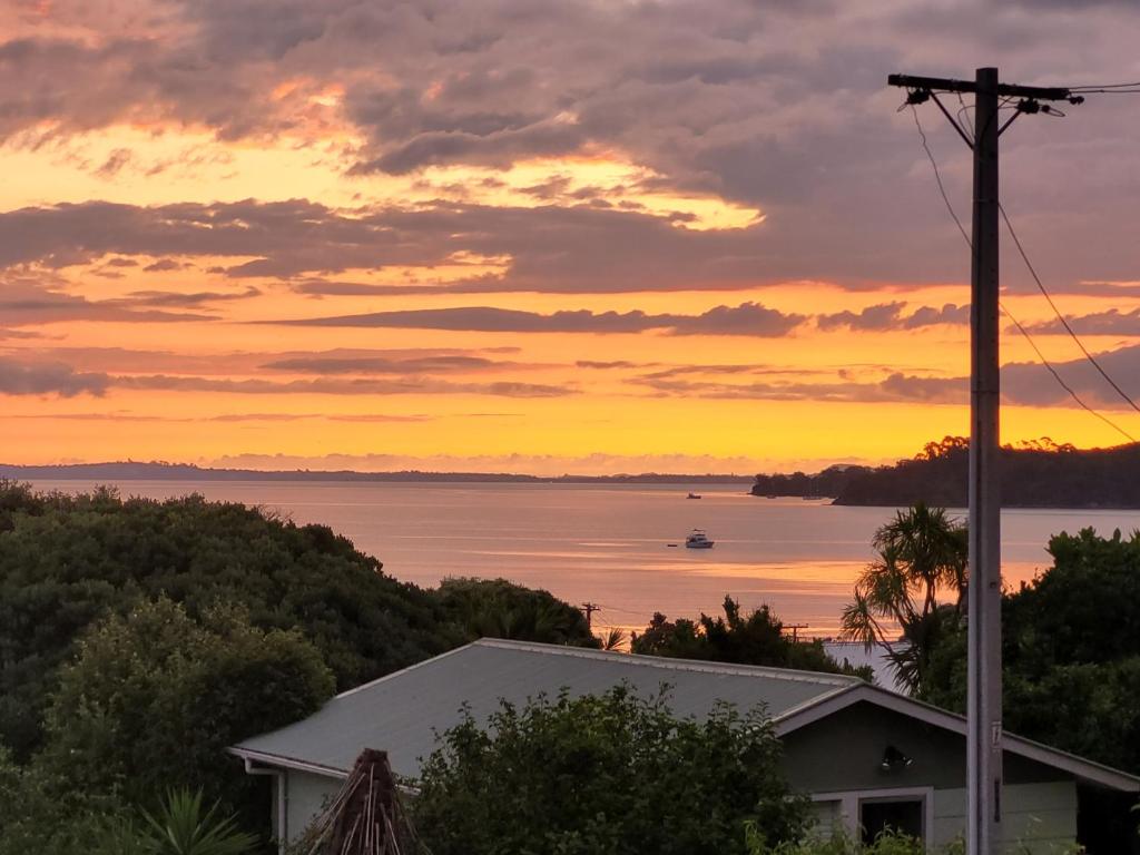 a sunset over the water with a house at Classic bach near the beach in Oneroa